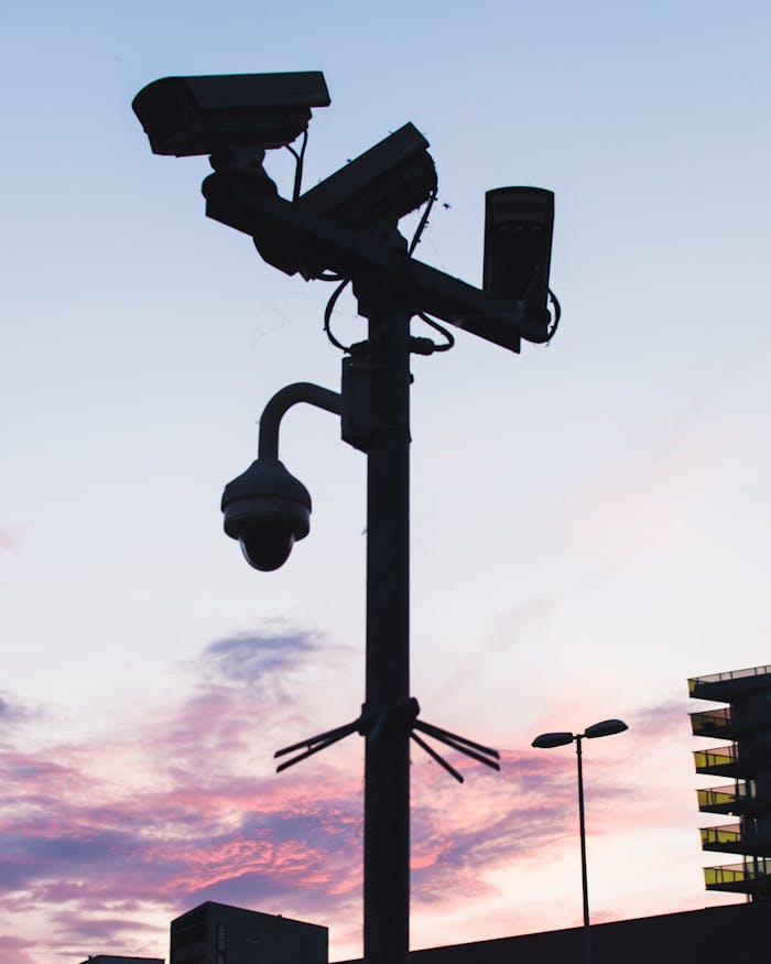 Silhouette of surveillance cameras and streetlights against a beautiful sunset sky.